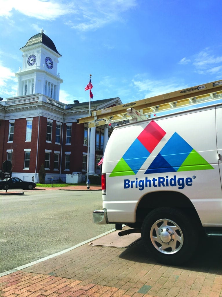 A BrightRidge service van is parked in front of a historic red-brick building with a clock tower under a clear blue sky.