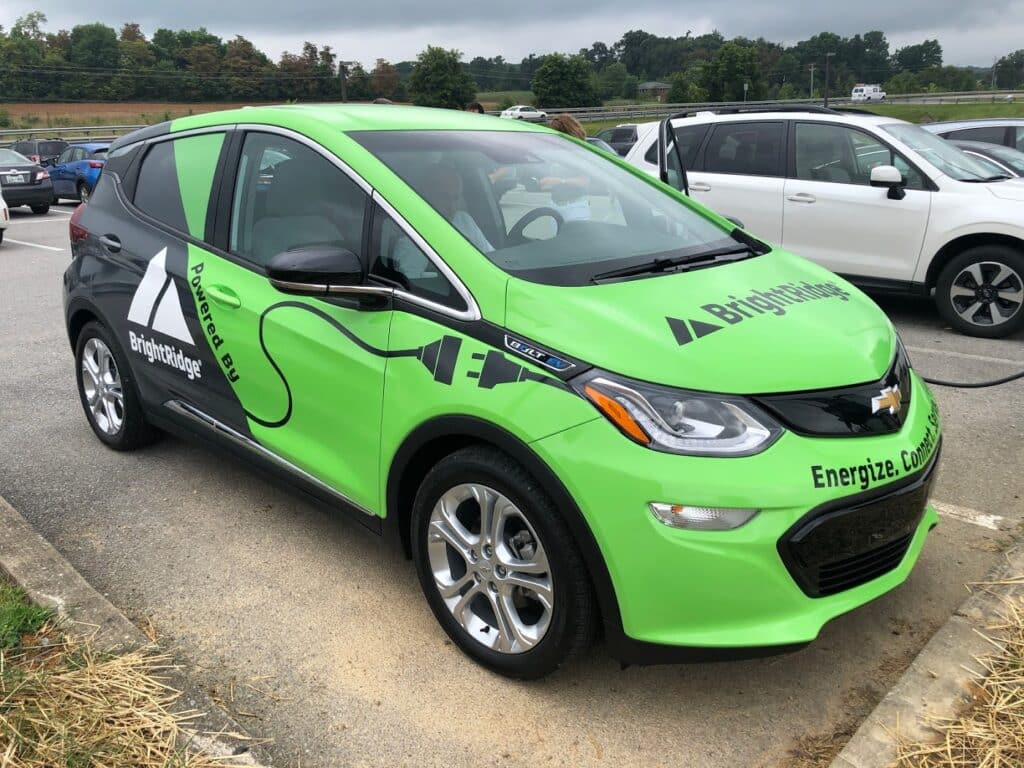 A green Chevrolet Bolt EV with BrightRidge branding on the side is parked in a lot, charging via a cable connected to the front.