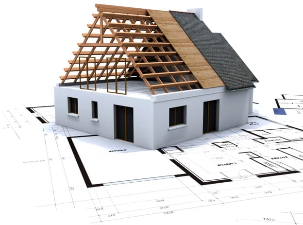 A partially constructed house model with exposed wooden roof framework on top of architectural blueprints.