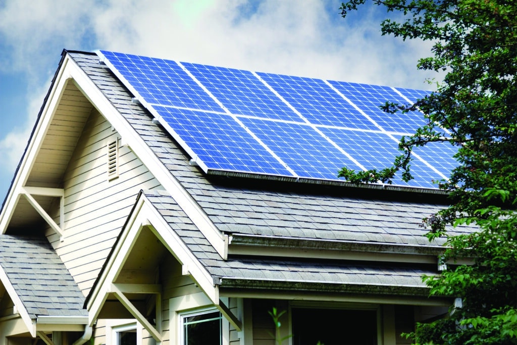 A house roof with installed solar panels alongside trees under a partly cloudy sky.