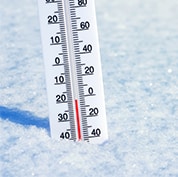 A thermometer reads below freezing temperatures, with the device partially embedded in snow.