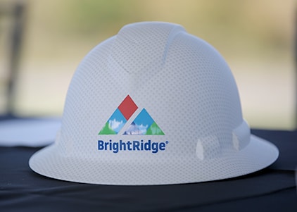 A white hard hat with the "BrightRidge" logo featuring a colorful triangle design is placed on a black surface.