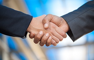 Two individuals in business attire shaking hands, symbolizing agreement or partnership, with a blurred blue and beige background.