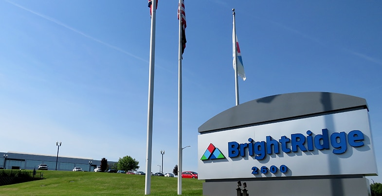 BrightRidge sign with logo and address 2600 stands in front of a green lawn, three flagpoles, and a large building under a clear blue sky.