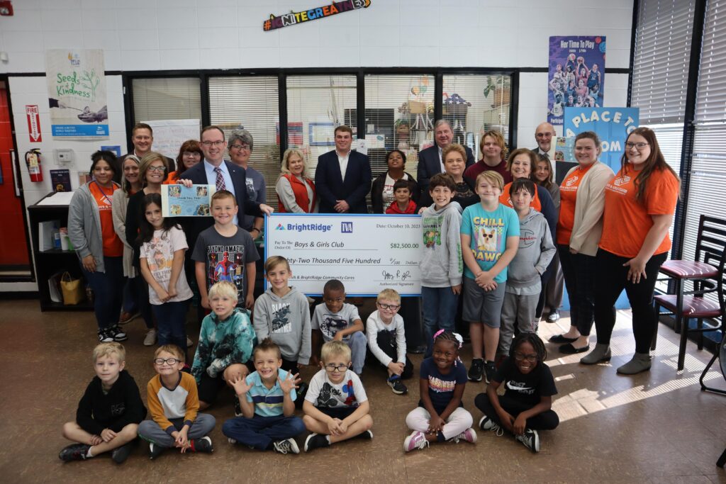A group of adults and children pose with a large check for $12,500 from BrightRidge to the Boys & Girls Club. The event takes place indoors, in a classroom or community center setting.