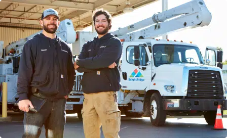Two BrightRidge workers smiling nd standing in front of bucket trucks.