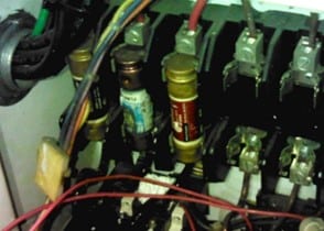 A close-up view of electrical fuses and wiring inside a circuit breaker panel.